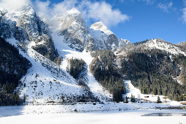 Majestic, snow-covered Alps rise above a frozen lake on a clear day. The winter landscape showcases nature's beauty, inviting exploration and wonder.