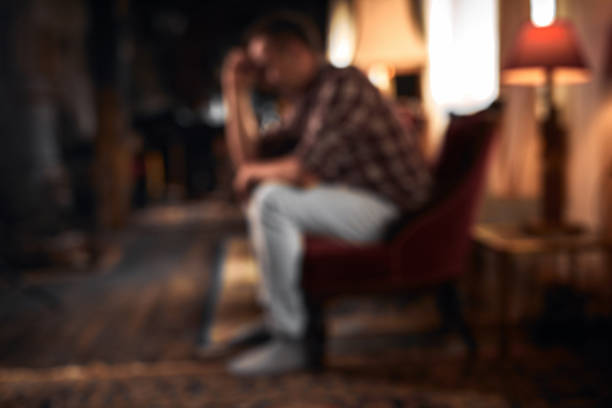 Man with headache, depression, sadness and loneliness sitting on a chair at home. Out of focus photo suitable for backgrounds.