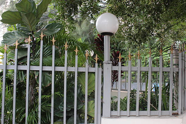 White wooden fence in the garden with green grass and water reflection.