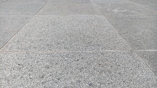 Close up perspective of a patterned gray tile floor with distinct grout lines, showcasing the rough, granular texture of the paving material