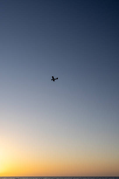 Peaceful seascape at golden hour with calm waves, warm sunset light and a small airplane silhouette flying across the sky. Minimalistic travel and freedom concept with copy space, ideal for tourism, lifestyle, aviation and background use.