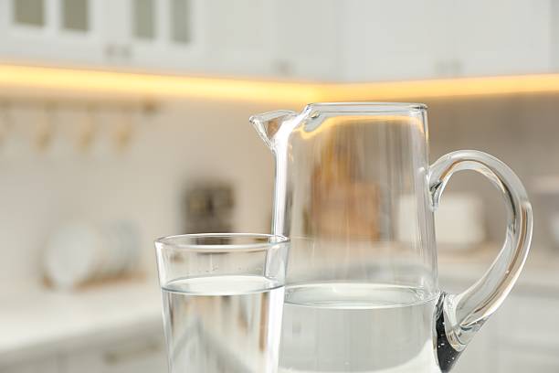 Jug and glass with clear water in kitchen, closeup