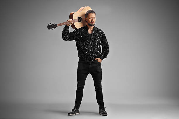 Young elegant man with an acoustic guitar over shoulder isolated on gray background