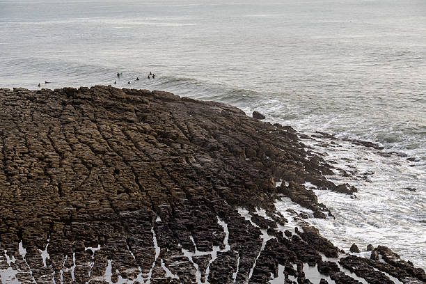 Estoril Portugal December 17 2025. Surfers wait beyond a rocky shoreline as small waves approach the Atlantic coast