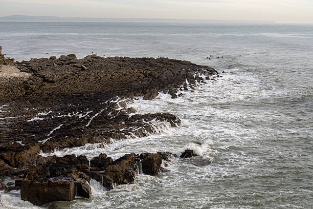 Estoril Portugal December 17 2025. Layered rock formations extend into the Atlantic Ocean along a rugged coastal shoreline