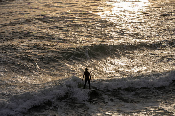 Estoril Portugal December 17 2025. A surfer rides a breaking Atlantic wave during sunset with golden light reflecting on the water