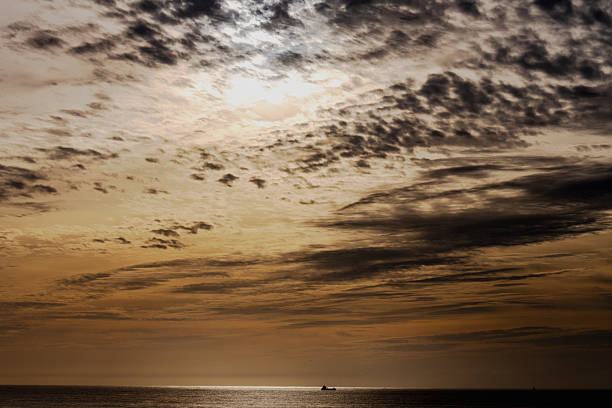 Golden and dark clouds stretch across the sky above the Atlantic Ocean with a small vessel near the horizon