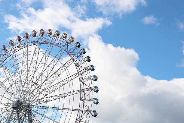 Colorful Ferris wheel gondolas against bright blue sky and clouds.