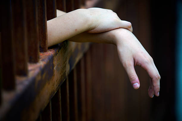 A close-up image of a relaxed human hand resting through rusty metal bars, capturing a melancholic mood. The interplay of light and shadow enhances the emotional depth.