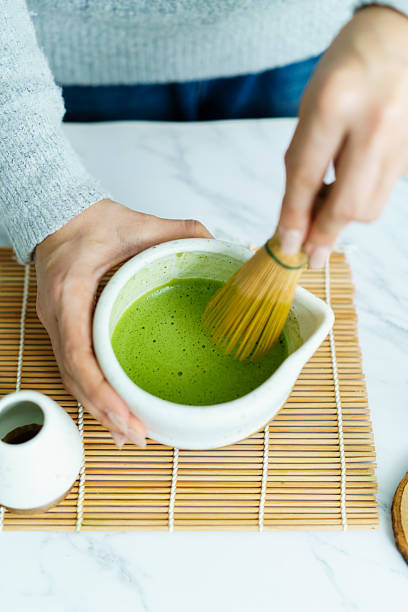 Hands whisking matcha green tea with bamboo whisk