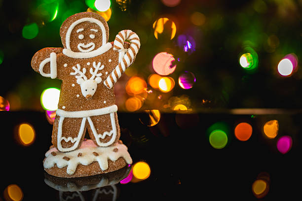 A portrait-style image of gingerbread cookie decorated with icing and a reindeer motif holding a striped candy cane. Set against blurred Christmas lights, the composition provides space for text overlays, ideal for greeting cards or editorial use.