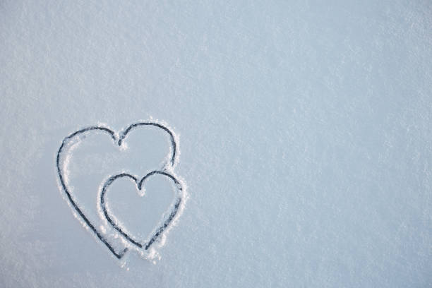 Two heart shapes on a white fresh snow in winter, close up. Valentines Day background