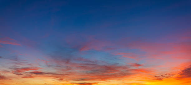 Vibrant Panoramic Sunset Sky with Dramatic Pink and Orange Clouds,A breathtaking panoramic view of a sunset sky featuring a vivid transition from deep blue to brilliant orange and pink hues, with soft wispy clouds scattered across the horizon.