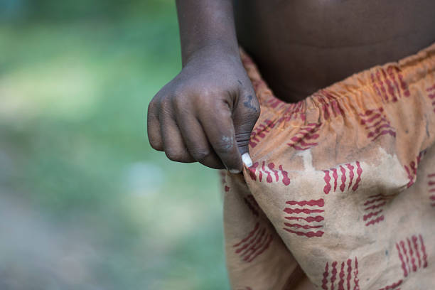 A detailed close-up captures a child's dark-skinned hand gently holding a tiny white object. The hand is near a piece of patterned fabric, suggesting simple clothing. The background is softly blurred