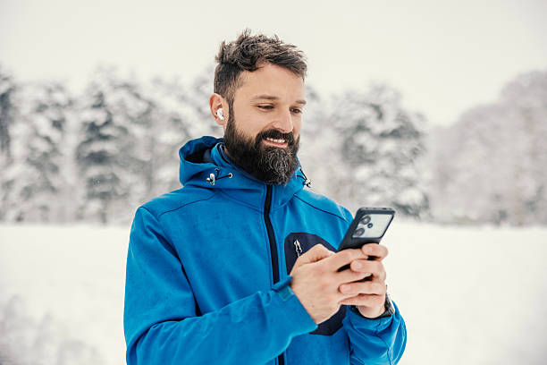 istock Man using smartphone and earbuds in snowy forest 2254926673