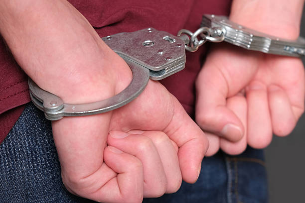 istock Hands bound behind, Restrained hands in metal cuffs, Arrest scene showing restrained hands and tense wrists, Dramatic scene of handcuffed hands behind back during detention 2254928222