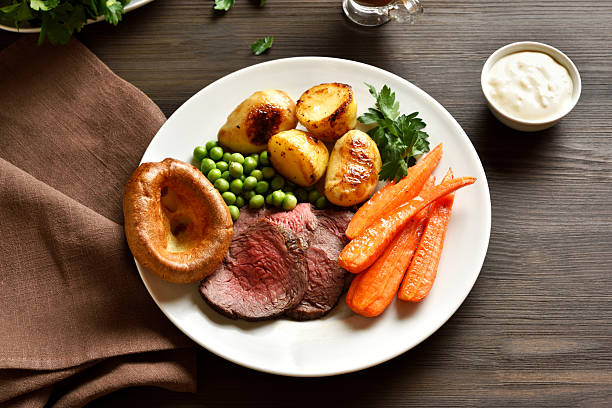 Close up view of sunday Roast with roasted beef, carrots, crispy potato, green pea and yorkshire pudding. Traditional british dish. Brown wooden background.