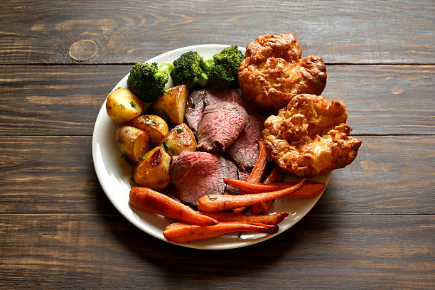Sunday Roast with roasted beef, carrots, crispy potato, broccoli and yorkshire pudding on brown wooden background. Traditional british dish.
