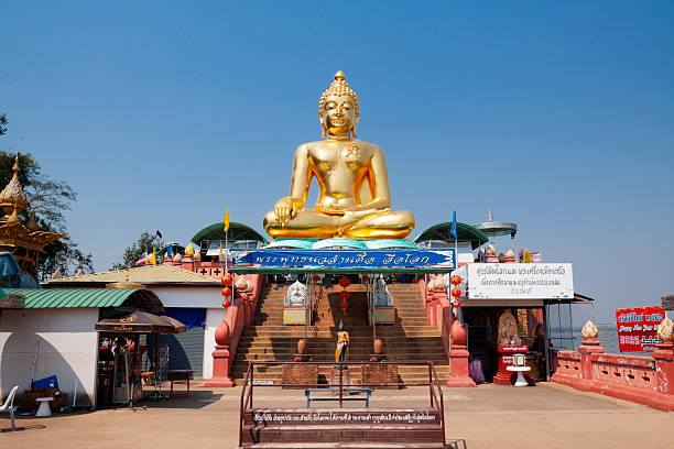 Big sitting thai buddha  on a platform at Mekong river at Golden Triangle between Myanmar, Thailand and Laos in Ban Sop Ruak. At left side is a kiosk. At right side is a shrine