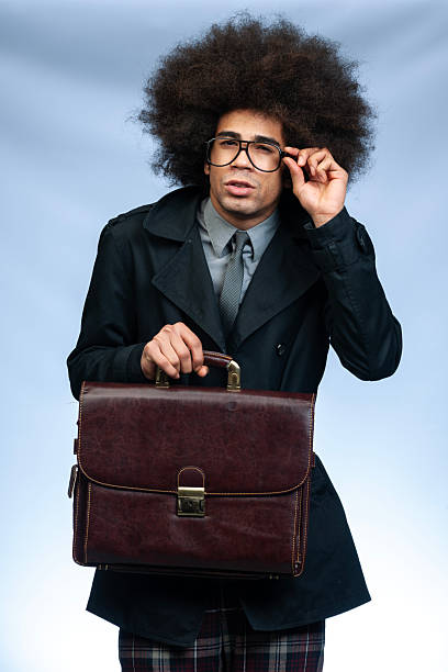 three quarter length shot of a nerdy businessman with big afro hair holding brown leather briefcase while documents staring to fall, camera on grey background