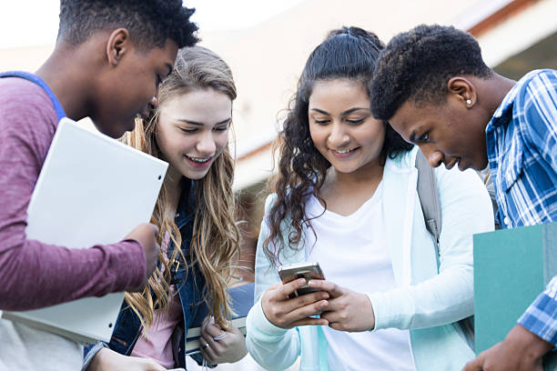 istock Diverse group of smiling teenagers collaborating outdoors while looking at a smartphone screen. 2254935809