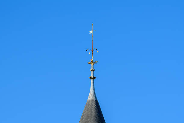 Close-up of a decorative metal spire with a weather vane atop a slate turret roof, set against a vivid clear blue sky at La Conciergerie in Paris.