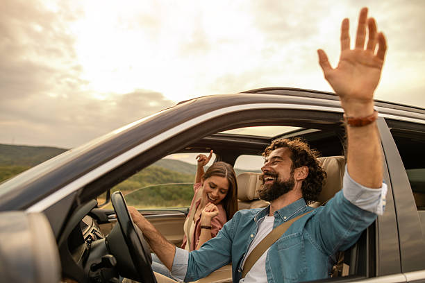 Young man in car on mountain road looks out from window car, outstretched arms for freedom. Mountain landscape in Summer, shot in Graubunden Canton, Switzerland.