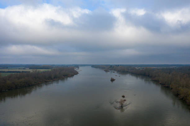 Aerial view of the Loire river winding between bare trees and open fields under a brooding sky near Dampierre. The muted winter tones and calm water create a peaceful, expansive atmosphere.