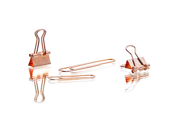Copper binder clips and paper clips arranged on a white reflective surface.
