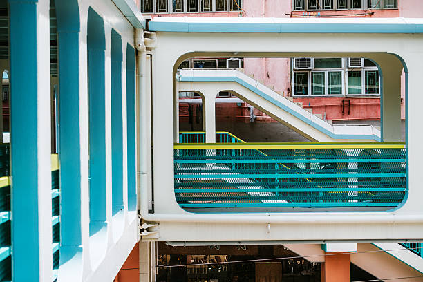 Vibrant multi-level walkways with blue railings and pastel staircases create an energetic, urban scene in Hong Kong. An architectural study of color, structure, and movement in a busy city setting.