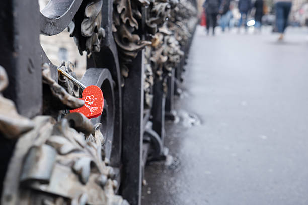 Heart-shaped love padlock hanging on a bridge railing in Paris, featuring a heart symbol and Paris inscription. Romance, travel memories, iconic city detail, love concept.