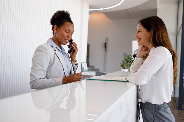 istock Receptionist speaking on a landline phone and taking notes, providing excellent customer service to a smiling client waiting at the reception desk 2254956082