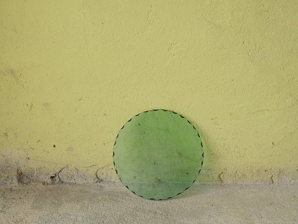 Round green disc leaning against rough plaster wall, minimalist abstract composition