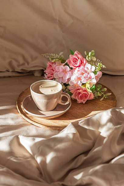 Cappuccino Cup and Flowers on Tray with Satin Bedding in Sunlight. Valentine's or Mother's Day Celebration
