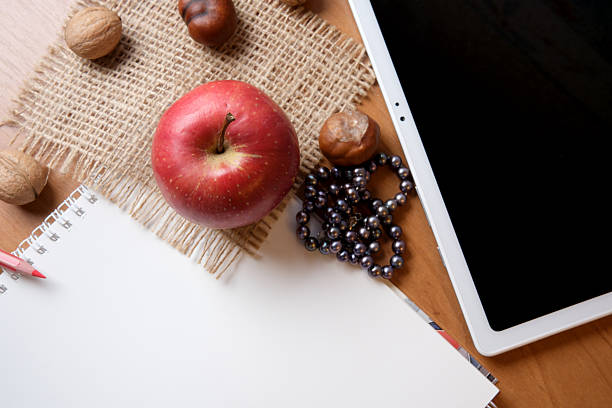A red apple rests next to a blank notebook and a tablet, with walnuts scattered around.