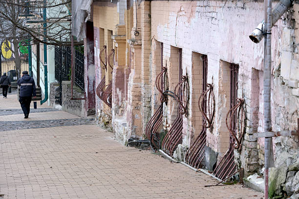 A person strolls past old brick buildings adorned with rusty metal details. Andreevsky Uzviz, Kyiv, Ukraine. December 8, 2025.