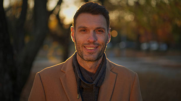 Smiling man standing outdoors in autumn park at sunset