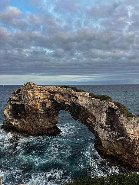 istock Natural rock arch over the sea with waves below 2254968092
