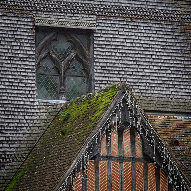 Moss covered rooftop and a Gothic-style window on historic timber-framed buildings in the old town of Honfleur, Normandy, France. Detail of traditional Norman architecture with weathered wooden shingles, mossy rooflines, and medieval window patterns in Honfleur.