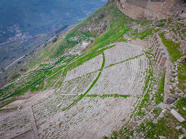 The Great Theater of Pergamon, the steepest in antiquity, was built by the Attalid Dynasty under King Eumenes II during the Hellenistic era in the 2nd century BC on the Acropolis overlooking Bergama. This high-resolution aerial capture reveals sharp focus on weathered stone seats, vivid greens of overgrown slopes, and dramatic lighting accentuating intricate ruins against mountainous backdrops.