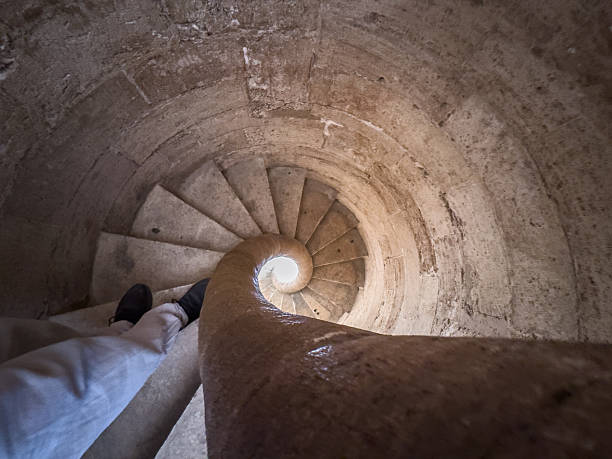 Into the vortex: descending a worn stone spiral staircase, feet hugging the edge.