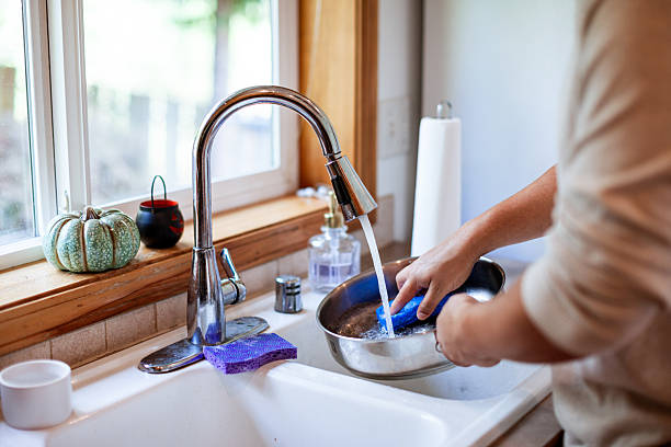 Close up of an unrecognizable person washing dishes by hand using a clean sponge and soap with water.