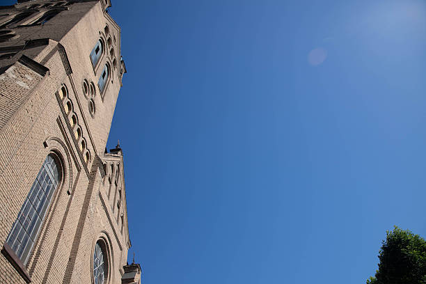 Reggio Emilia, Italy, 01.04.2025. Pointed Gothic church spire framed by rustic yellow buildings and clear blue sky