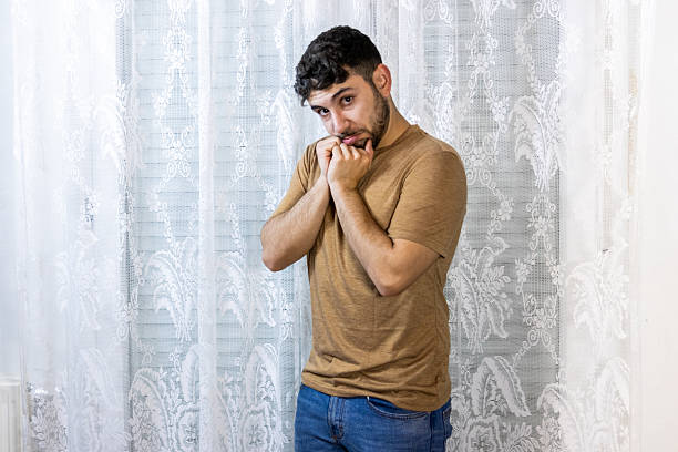 Young man standing indoors, expressing shyness or discomfort