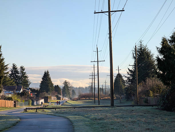 Surrey, Canada - January 5, 2026: Looking east on the Green Timbers Greenway in the Fleetwood-Tynehead neighbourhood. Pedestrians walk the path between the detached houses on 95A Avenue and the grass area. Rows of utility poles line the east-west easement. Winter morning with light fog over Metro Vancouver.