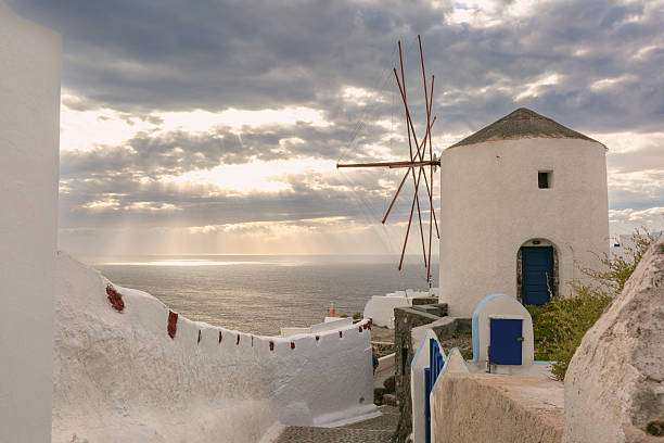 Historic white windmill overlooking the Aegean Sea in Oia village on Santorini island, Greece at sunset.