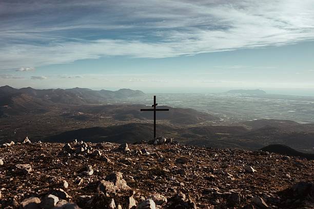 panoramic view from the top of the mountain with a cross in the center and in the background the landscape with the sea on the horizon at sunset. Shot in the Lepini Mountains, Lazio, Italy.