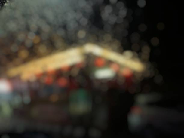 Blurred image of a house seen through a rain-covered window at night, glowing with warm lights.