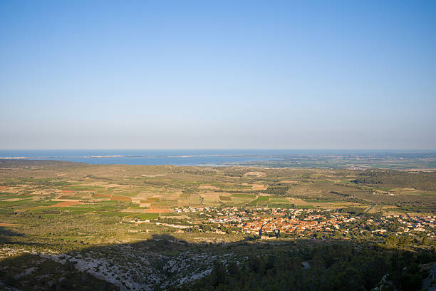Wide view over patchwork fields, a small village, and the distant blue Mediterranean coastline under a clear sky near Opoul Perillos.