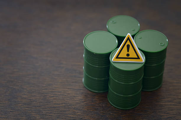Hazard warning concept with miniature barrels and exclamation sign on textured dark background.